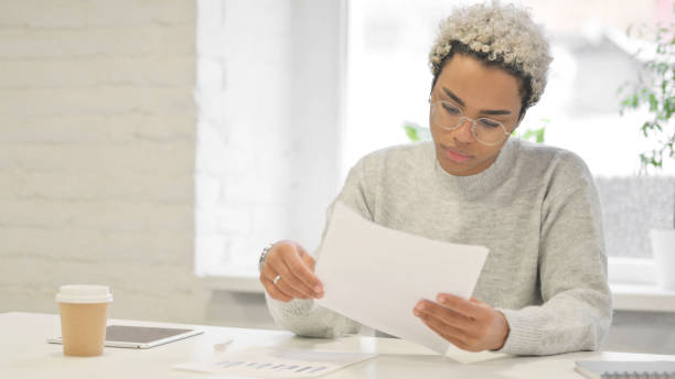 istock African Woman Reading Reports while Sitting in Office 1363452118