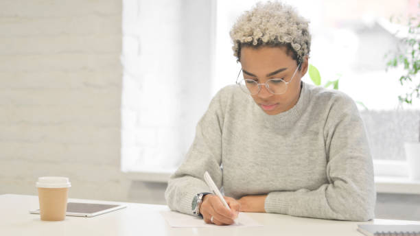 istock African Woman Thinking while Writing on Paper in Office 1363452212