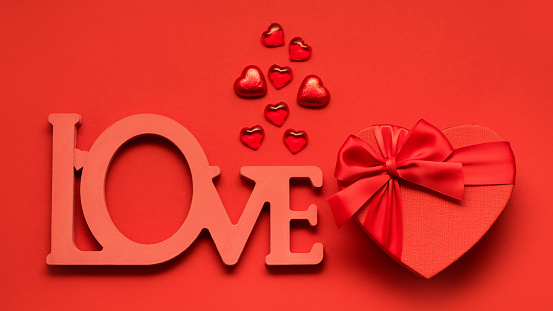 Valentine's day or Wedding romantic concept and word love. Red festive box and chocolates on red background. Top view, flat lay, copy space
