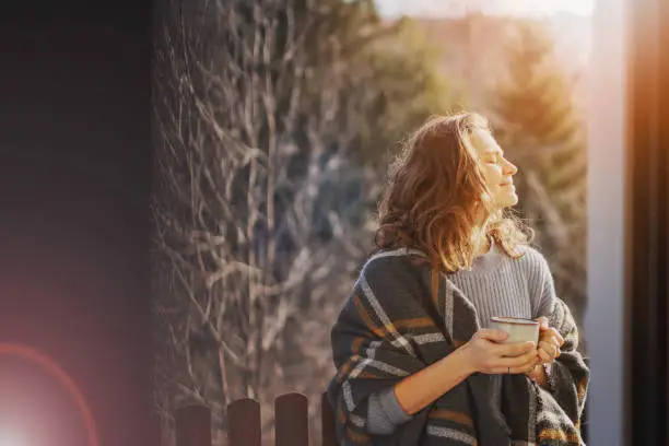 Photo of Happy cheerful beautiful curly young woman enjoying morning coffee and nature view on the terrace of a country house