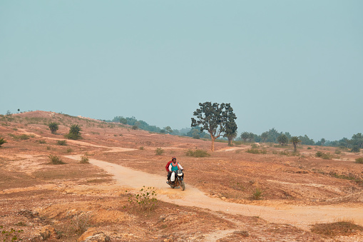 Bihar, 12/11/2021: Local people riding motorcycle through dusty track, amidst rustic nature at Simultala (or Shimultala), where the landscape is mostly dry. This entire area lies within Chota Nagpur plateau. Most part of this vast area remains uninhabitable with absence of local people.