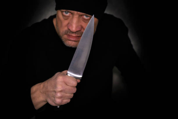 istock Aggressive man in the dark, holding a large kitchen knife in his hand. 1363464437
