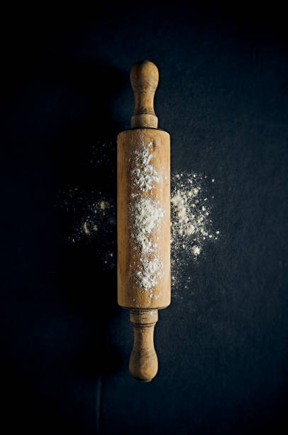 Old rolling pin with flour on dark background. Top view stock photo