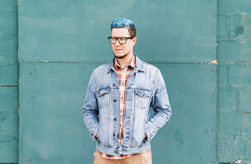 Handsome man in jeans jacket standing on a blue color wall background.