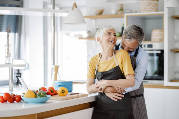 Romantic mature couple dancing in the kitchen Portrait of mature couple in the kitchen, dancing and having fun while preparing a meal middle aged couple dancing stock pictures, royalty-free photos & images