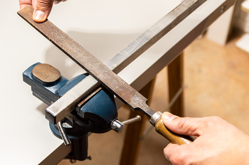 El hombre trabaja con tubería de hierro o raspa de lima de aluminio metálico agarrada en vise en la mesa del banco de trabajo photo