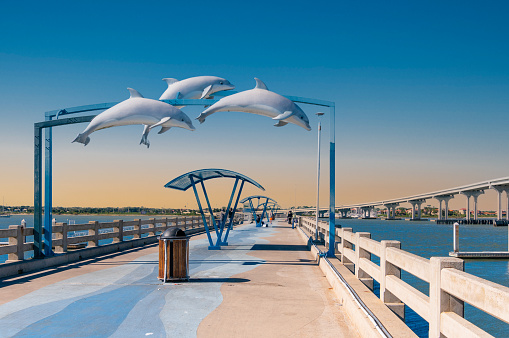Vilano Beach, Florida, USA -January 3, 2022-  A statue featuring three dolphins is suspended over the Vilano Beach fishing pier as a few people  gather in the background.