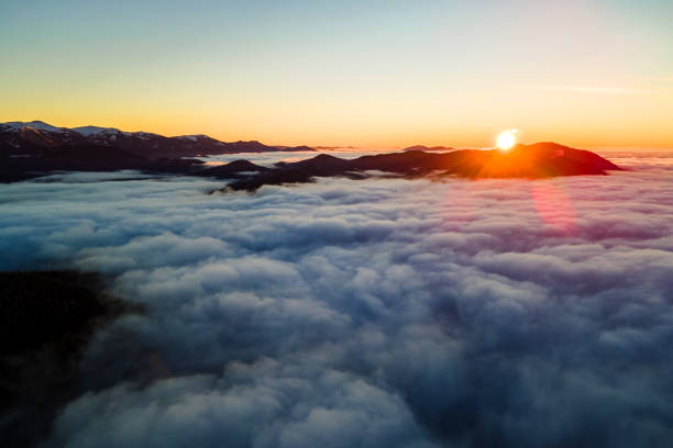 istock Aerial view of vibrant sunrise over white dense clouds with distant dark mountains on horizon. 1363475607