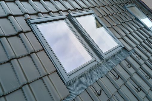 Closeup of attic window on house roof top covered with ceramic shingles. Tiled covering of building.