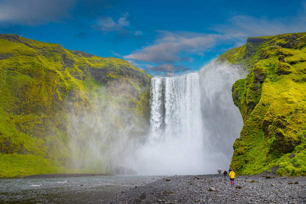 istock Powerful and famous Skogafoss waterfall with a lonely standing person in orange jacket, while hiking in Iceland, summer, scenic dramatic view at sunny day and blue sky. 1363476843