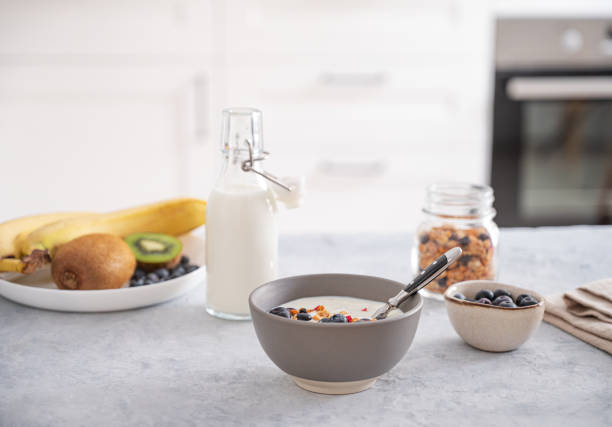 le concept d’un petit-déjeuner sain composé de yaourt végétarien, de granola et de fruits frais sur une table bleue sur fond de cuisine blanc. vue de face - yogurt greek culture milk healthy eating photos et images de collection