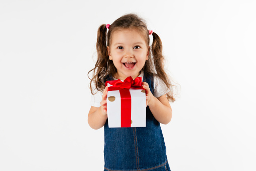 Cute little girl is holding a red gift box in her hands an is looking at camera with a nice smile.