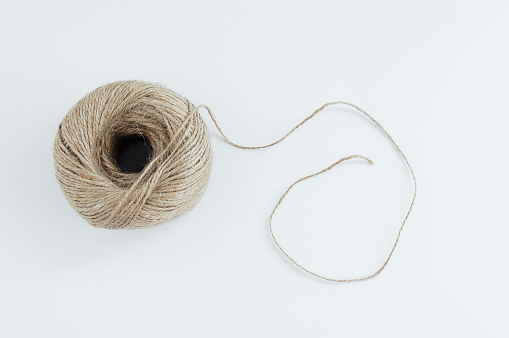 A skein of brown twine with a loose thread on a white background. A ball of jute twine. View from above.
