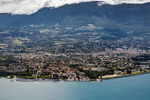 Color landscape photography of a high angle view over Aix Les Bains cityscape, famous thermal station city and marina in summer. This image was taken on Bourget Lake riverbanks, in Savoie in Alps, Auvergne-Rhone-Alpes region in France, Europe.