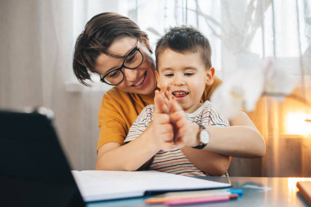 caucasian mother sitting at a table at home helping her son with his homework showing him something, using laptop. online education. studying, doing homework. - 2113 imagens e fotografias de stock