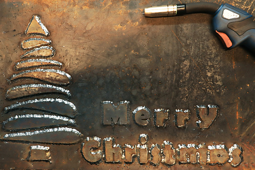 A steel sheet of metal on which a Christmas tree is welded and the phrase Merry Christmas. Christmas card for workers in heavy industry and metalworking.