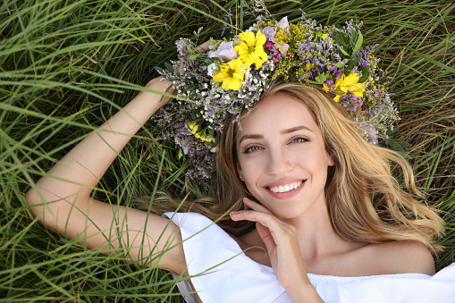Young woman wearing wreath made of beautiful flowers on green grass, top view