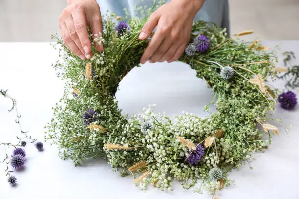 Woman making beautiful wreath of wildflowers at white table, closeup