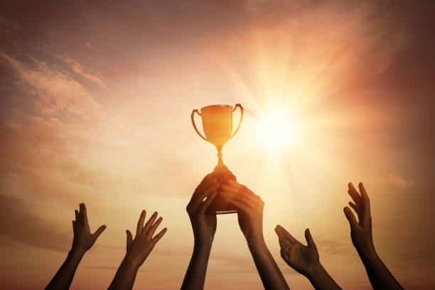 istock Winning team with gold trophy cup against shining sun in sky 1363487638