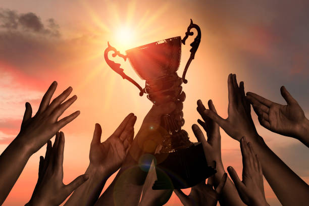 istock Winning team with gold trophy cup against shining sun in sky 1363488733
