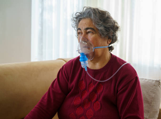 istock Senior woman doing inhalation through oxygen mask at home 1363489256