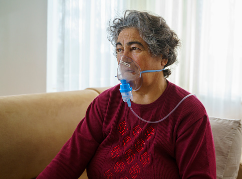 Senior woman doing inhalation through oxygen mask at home