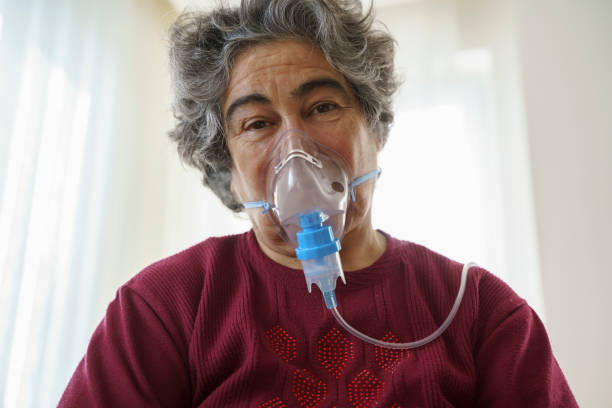 istock Senior woman doing inhalation through oxygen mask at home 1363489345