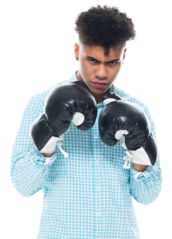Waist up of aged 18-19 years old with curly hair african ethnicity young male standing in front of white background wearing boxing glove who is in concentration and boxing who is fighting