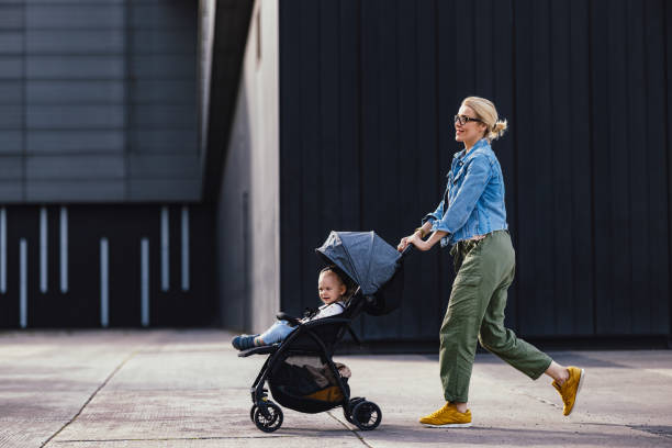 alegre madre en un paseo por la ciudad empujando a su hija en un cochecito - pushing women wall people fotografías e imágenes de stock