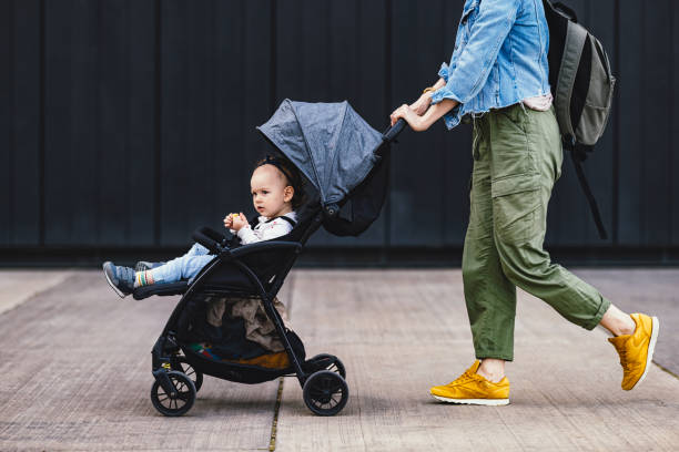 anonyme mutter auf einem stadtspaziergang schiebt ihre tochter in einem kinderwagen - sportkinderwagen stock-fotos und bilder