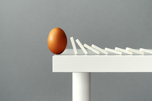 Egg on the edge of a table about to fall due to domino tiles pushing each other