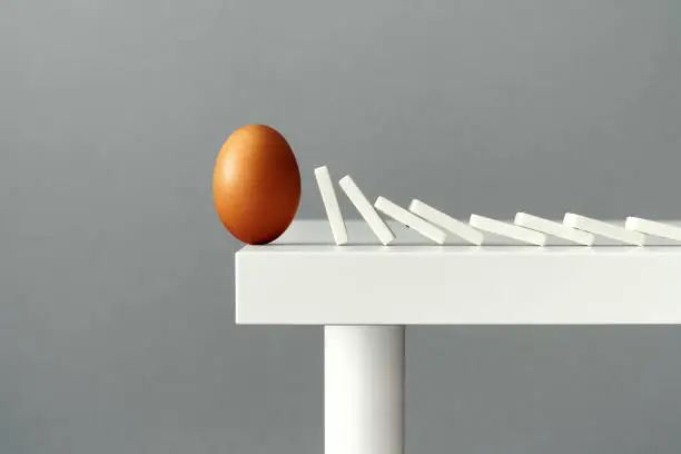 Photo of Egg on the edge of a table about to fall due to domino tiles pushing each other