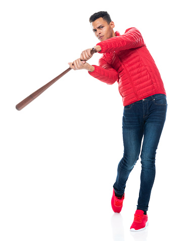 Full length of aged 20-29 years old with short hair african ethnicity male standing in front of white background wearing jacket who is serious who is hitting and holding baseball bat