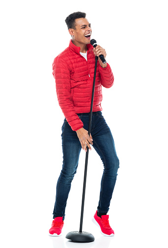 One person of aged 20-29 years old with black hair african-american ethnicity young male singer dancing in front of white background wearing blazer who is singing and holding microphone stand