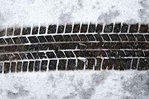 Above view of a car tire track on the snow covering the asphalt on the street in winter day close up