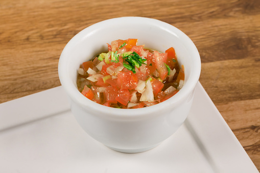 Vinagrete or Vinaigrette is a traditional Brazilian sauce made with tomato, pepper, onion, vinegar and parsley. Served in white bowl on wooden background.