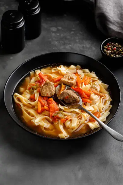 Photo of Lagman. The national Uzbek soup with noodles and pieces of meat, fried vegetables. Close up soup. Black plate and black background