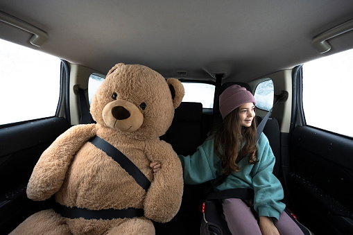 Road trips with children. Childhood travel themes. Girl with a giant teddy bear on a car trip.