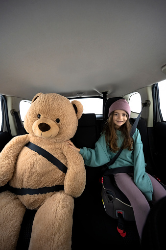 Road trips with children. Childhood travel themes. Girl with a giant teddy bear on a car trip.
