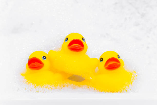 istock Pyramid of three yellow rubber duck for bathing in the bathroom among relaxing bubble baths, front view, copy space for advertising text. Home spa procedures 1363522381