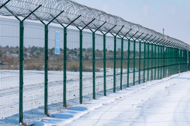 clôture en fer avec des barbelés dans un champ d’hiver enneigé contre un ciel bleu. territoire surveillé clôturé, pas d’accès. protection de la zone et lutte contre l’entrée illégale - winter wire barbed wire protection photos et images de collection