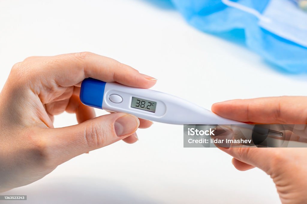Woman hands holding a medicine digital thermometer with high body temperature measurement on light background. Fever, flu illness and coronovirus desease symptoms concept Woman hands holding a medicine digital thermometer with high body temperature measurement on light background. Fever, flu illness and coronovirus desease symptoms concept. Fever Stock Photo