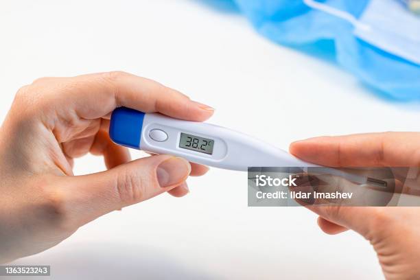 Woman Hands Holding A Medicine Digital Thermometer With High Body Temperature Measurement On Light Background Fever Flu Illness And Coronovirus Desease Symptoms Concept Stock Photo - Download Image Now