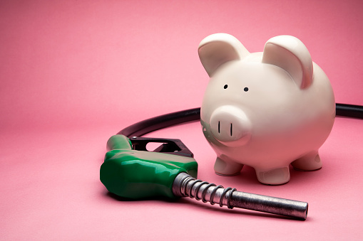 Concept Photo of a White Large Piggy Bank on Pink Background with Gas Nozzle