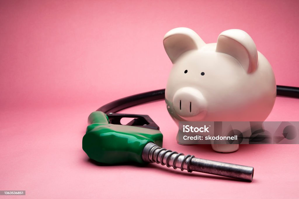 Concept Photo of a White Large Piggy Bank on Pink Background with Gas Nozzle This is a photo of a large white piggy bank on a pink background. This is a concept photo related to finance and money at the gas station. Gasoline Stock Photo