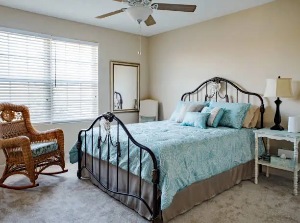 Bedroom with iron bed, wicker rocking chair decorated in blues, cream and beige.