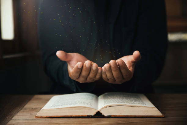 le mani di un bell'uomo stanno pregando per le benedizioni di dio su una bibbia aperta con la luce della finestra prega al mattino. potere di speranza o amore e devozione. - religious text god christianity men foto e immagini stock