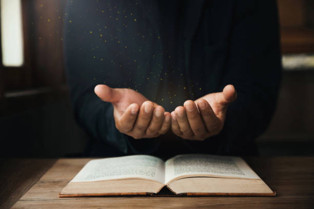 Handsome man hands are praying for God's blessings on an open bible with window light Pray in the Morning. Power of hope or love and devotion. stock photo