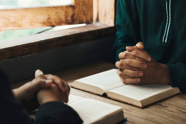 gutaussehende männerhände beten um gottes segen auf einer offenen bibel mit fensterlicht beten sie am morgen. kraft der hoffnung oder liebe und hingabe. - praying men god kneeling stock-fotos und bilder