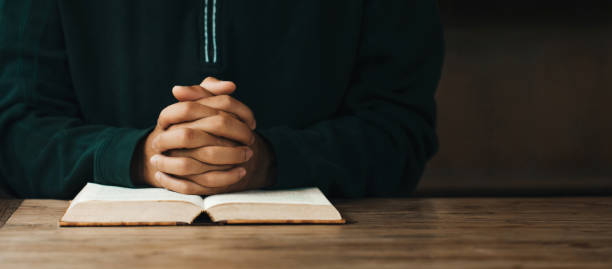 mãos do homem entrelaçadas na bíblia sagrada no conceito da igreja para fé, espiritualidade e religião, mão do homem com orações bíblicas. dia mundial de oração, dia internacional de oração, espaço para texto. - praying men god kneeling - fotografias e filmes do acervo